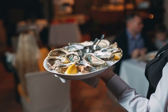 A waiter holds a serving of oysters. - Image by David Tadevosian / Shutterstock.com